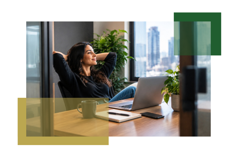A woman sits at a desk with a laptop, notebook, and coffee mug, smiling and leaning back with her hands behind her head, looking out a window overlooking a cityscape.